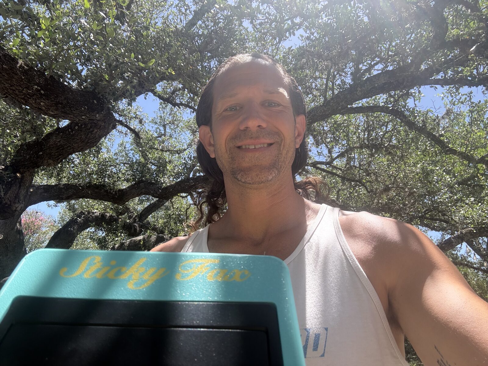 Dan, grinning under a Texas live oak, holding a teal-green-and-marigold StickyFax