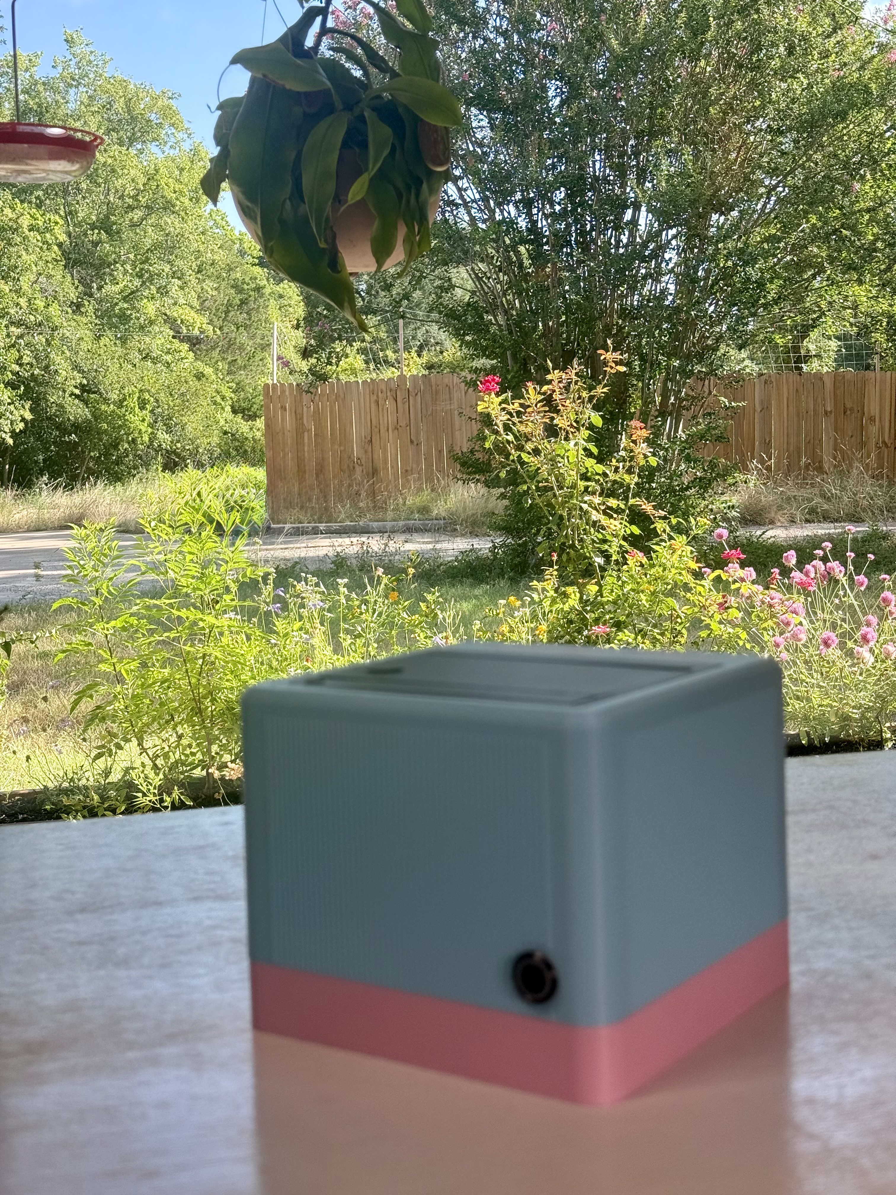 A teal-and-pink StickyFax on a patio table in front of a sunny wildflower garden