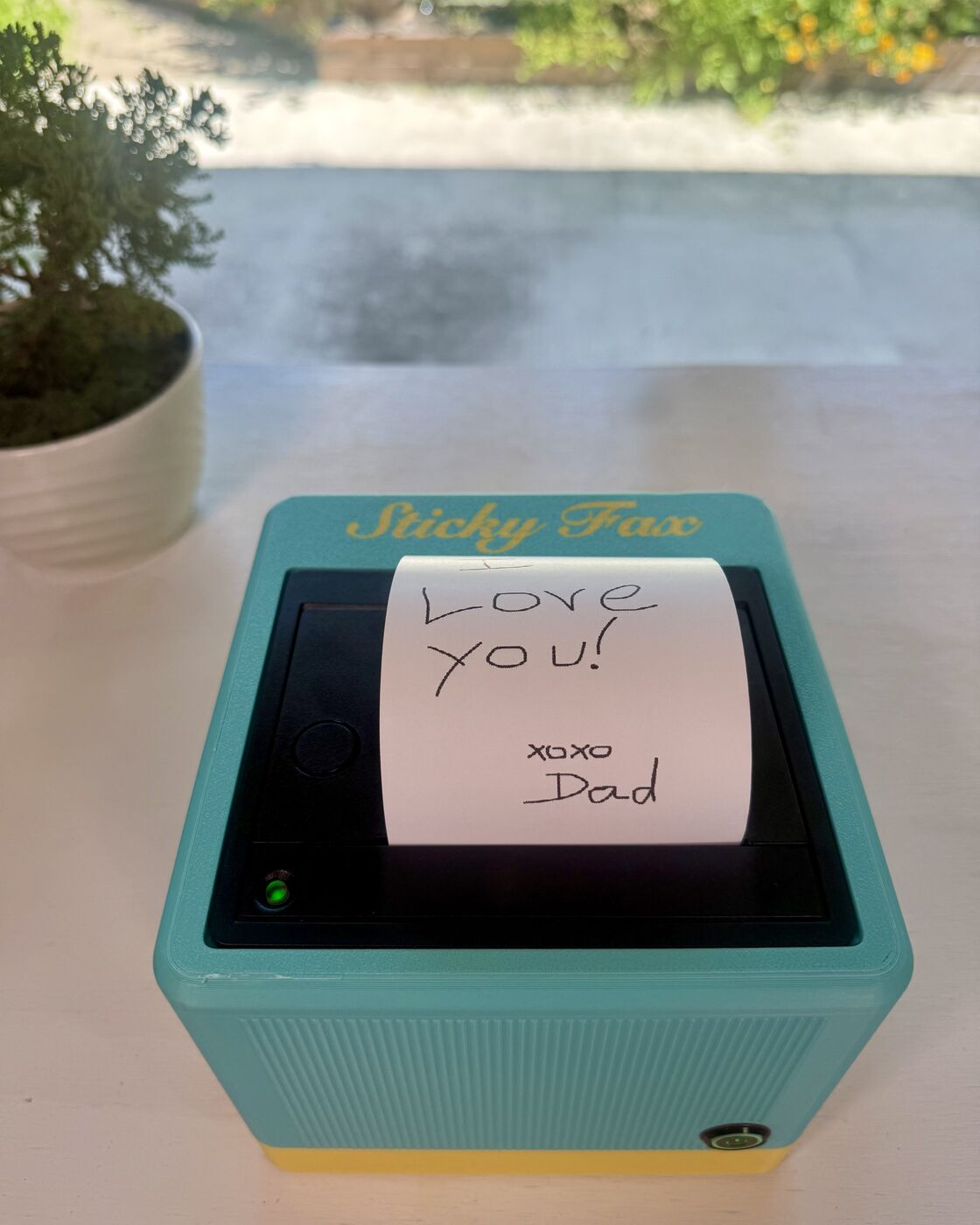 The tail of a printed fax standing in the printer slot — "xoxo, Dad" in handwriting